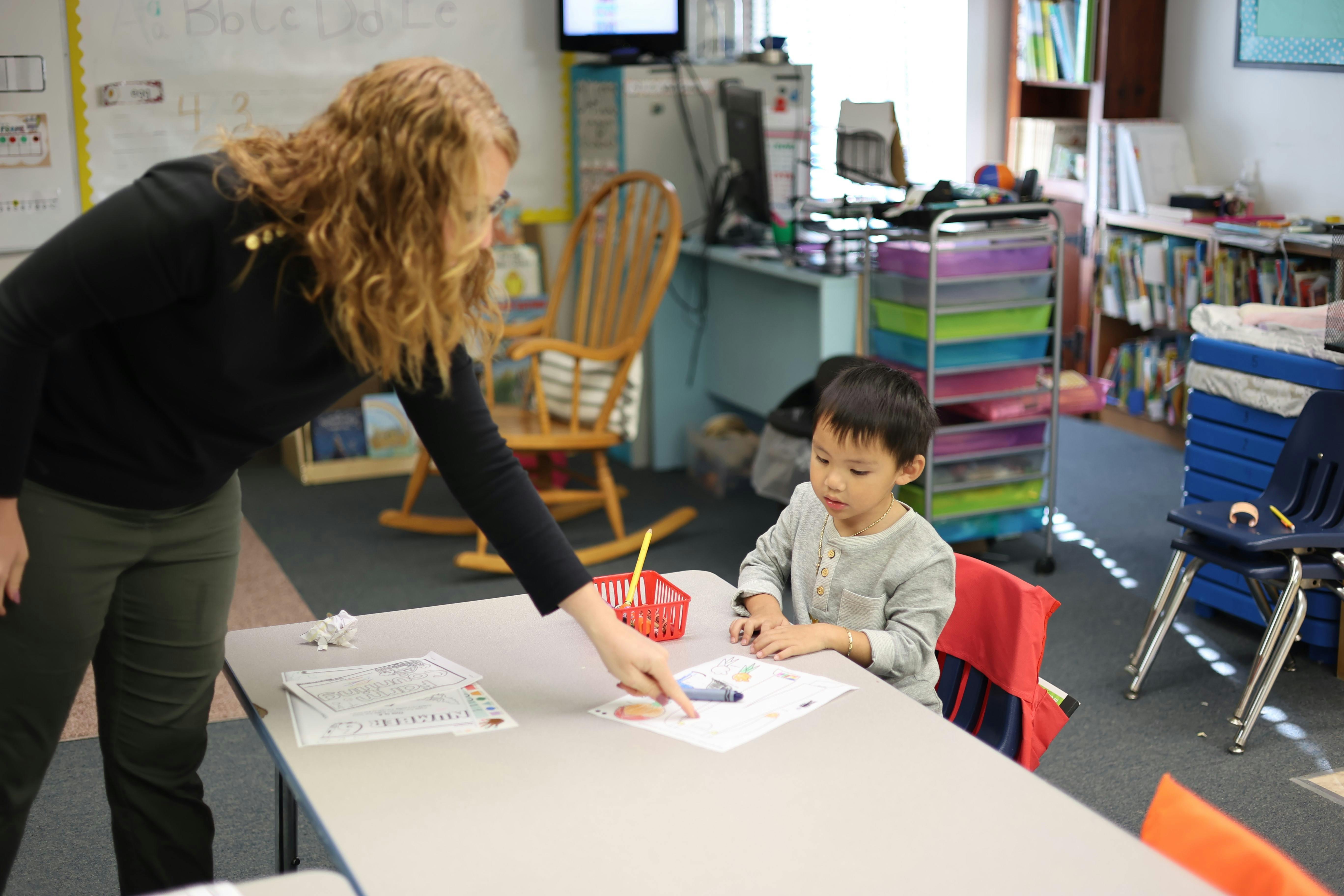 Person helping a child with an activity at a table in a classroom