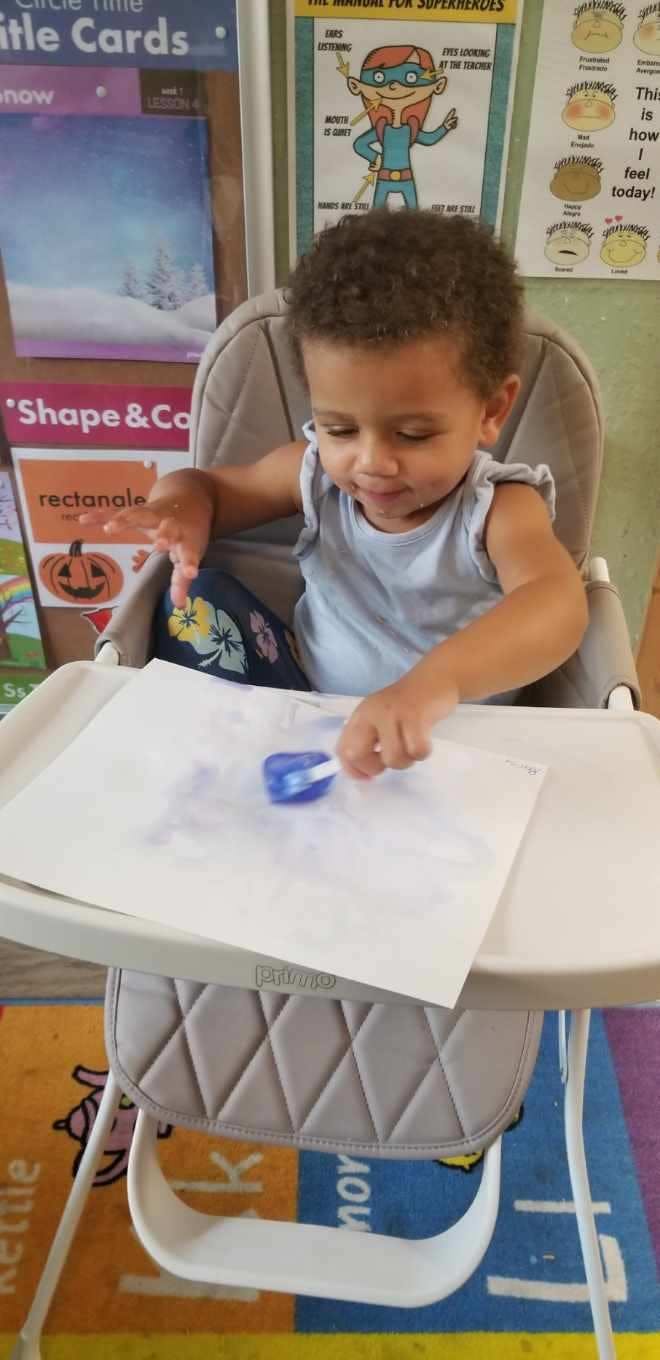 Child in a high chair painting on paper with a brush