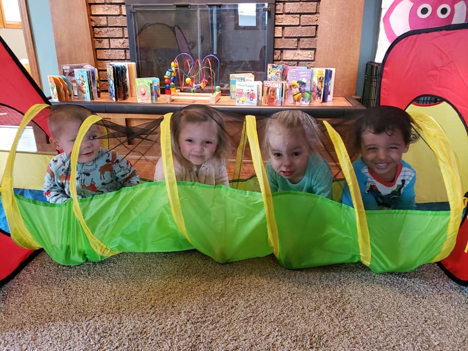 Four children playing in a green and yellow tunnel