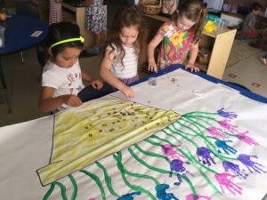Three children painting on a large sheet of paper