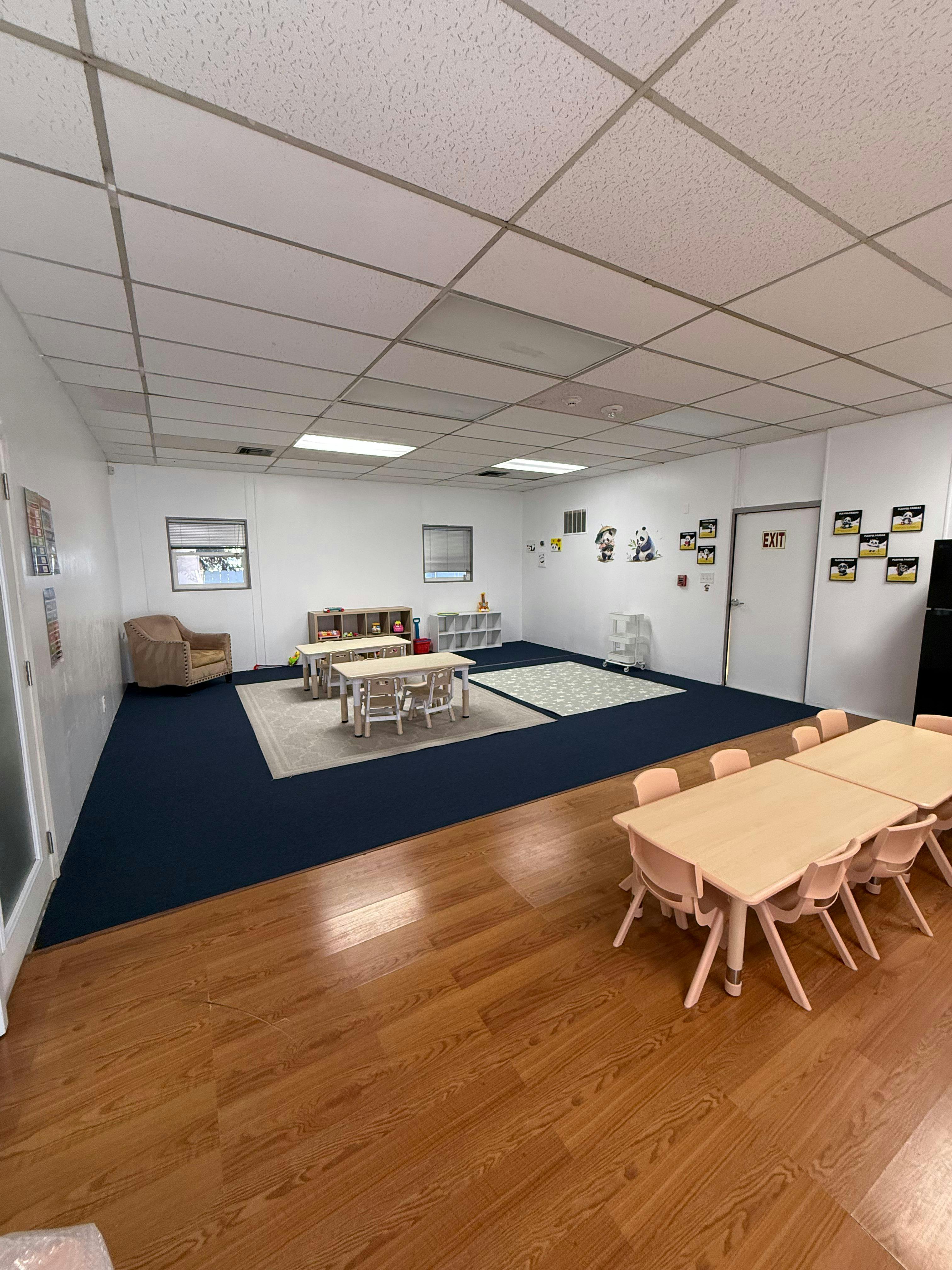 Classroom with child-sized tables and chairs, an armchair, and an exit door