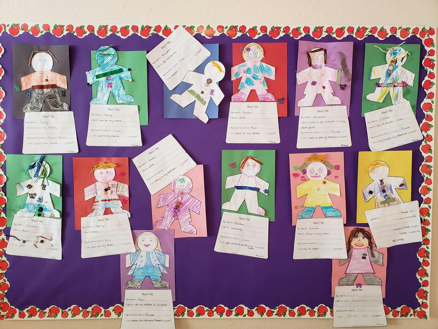 Children's paper doll crafts with written descriptions on a bulletin board