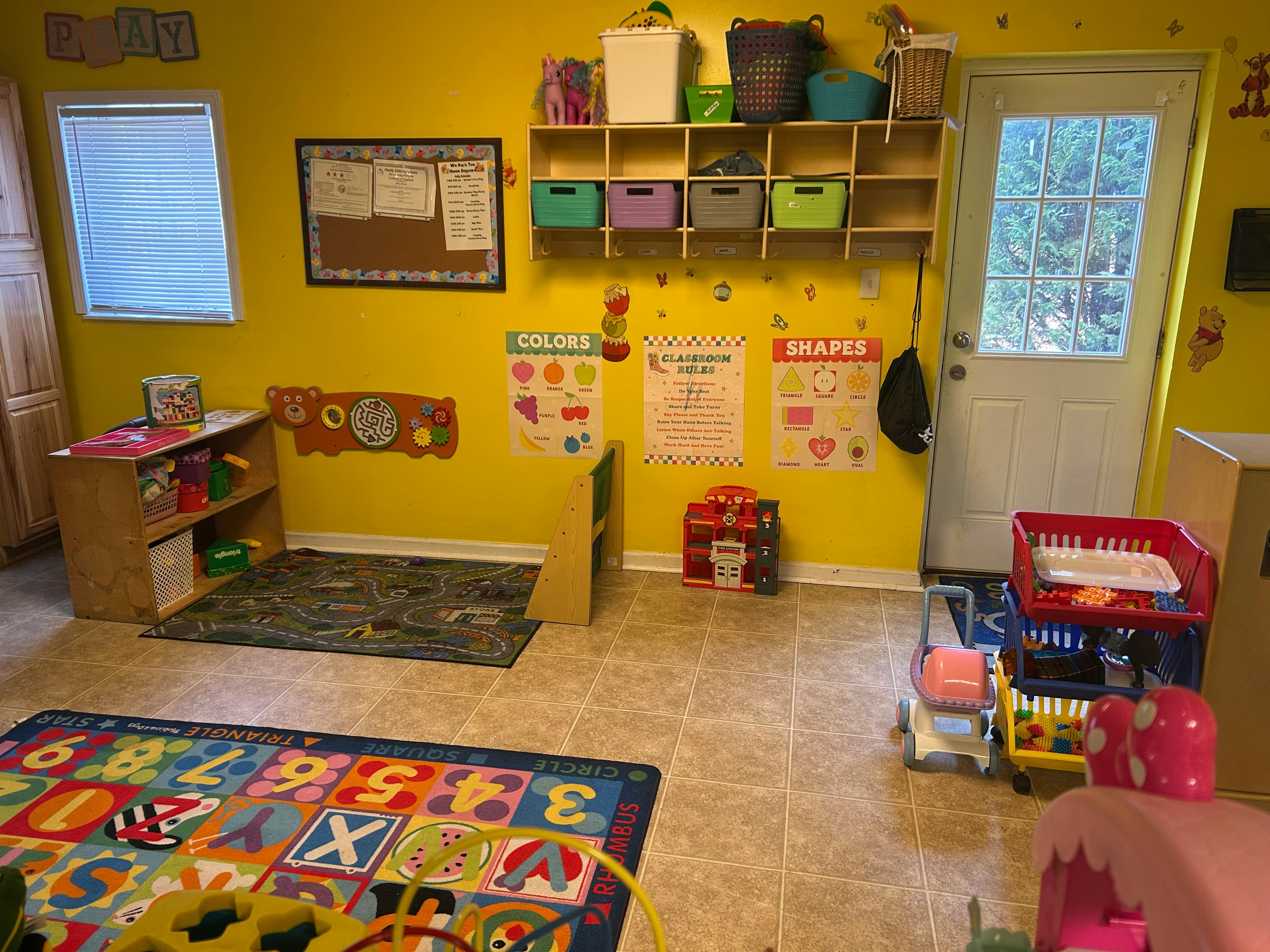 A classroom with yellow walls, shelves, and a colorful alphabet rug