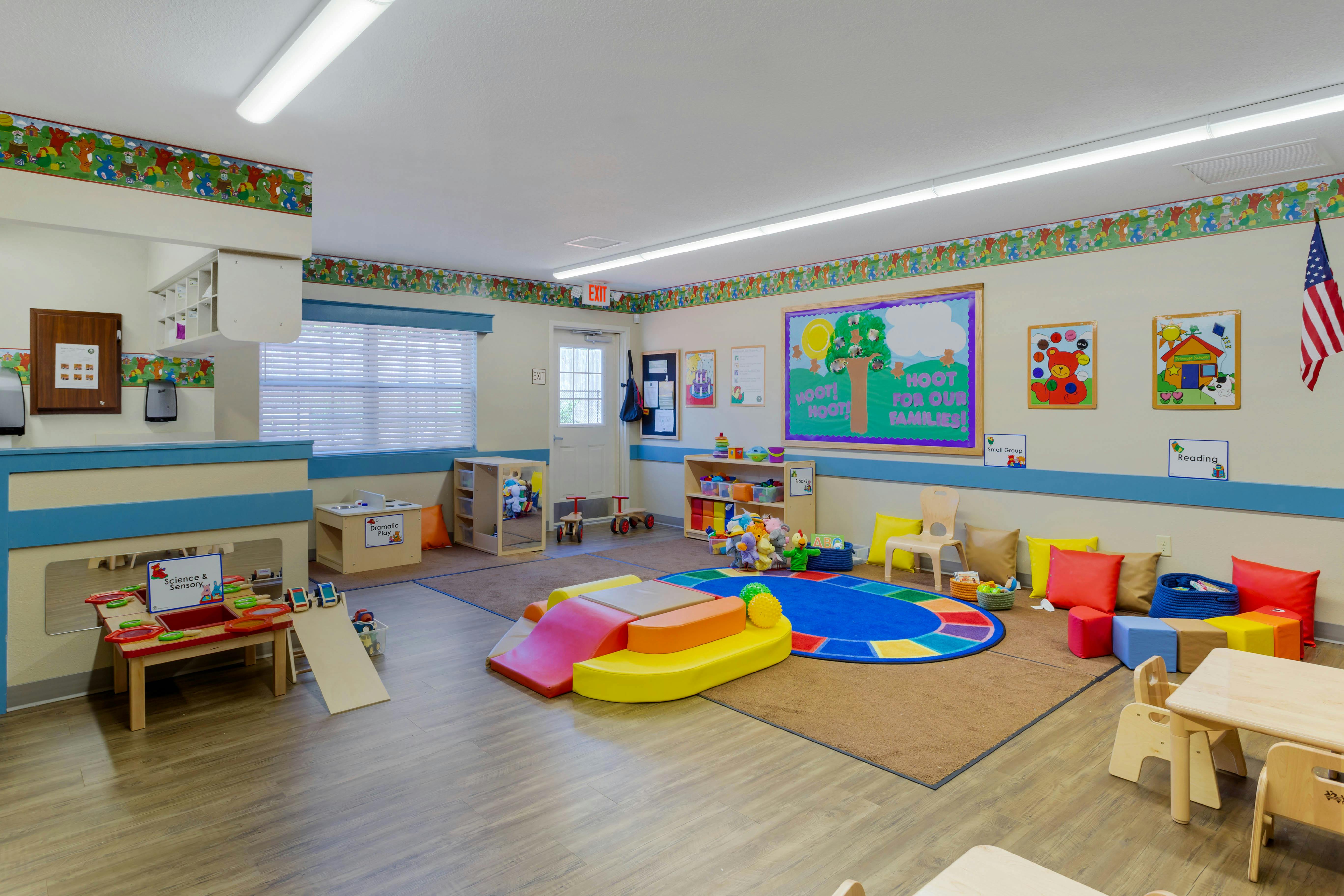 An empty early childhood classroom with various play areas and colorful rugs