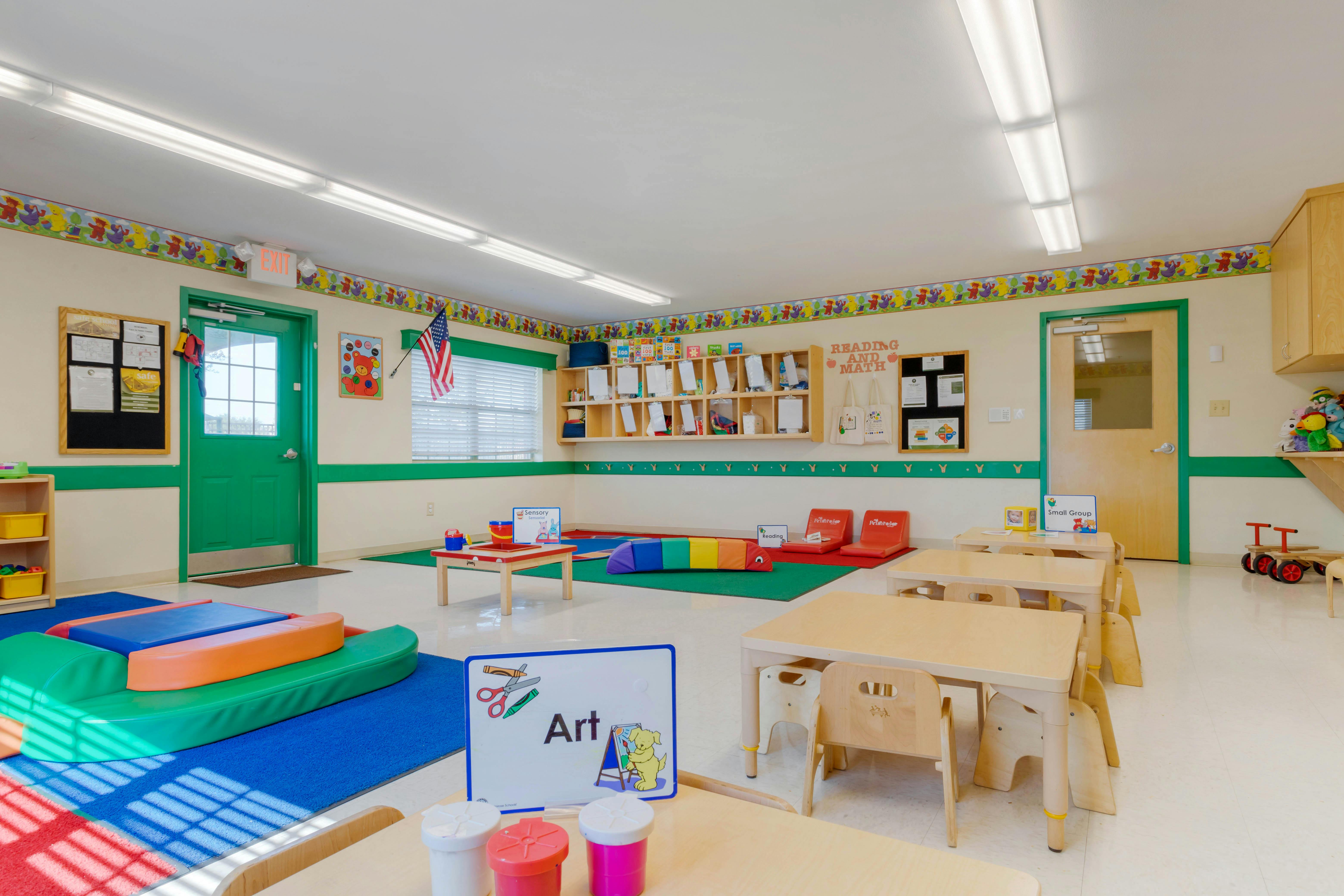 A colorful empty classroom with small tables, chairs, and play mats