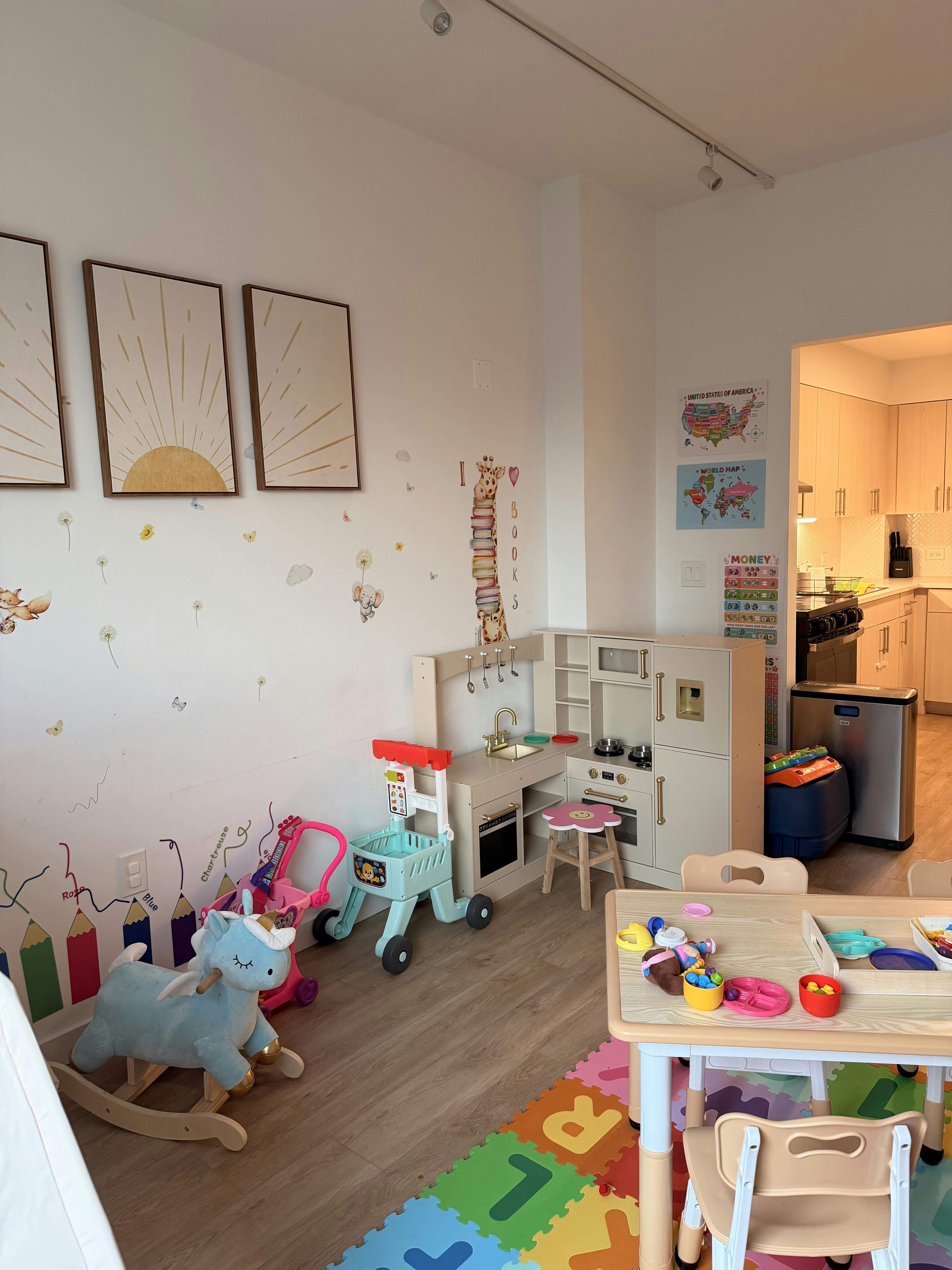 A children's play area with a toy kitchen, unicorn rocker, and table with toys