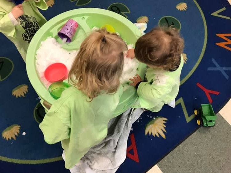 Two children playing with a sensory bin filled with white material