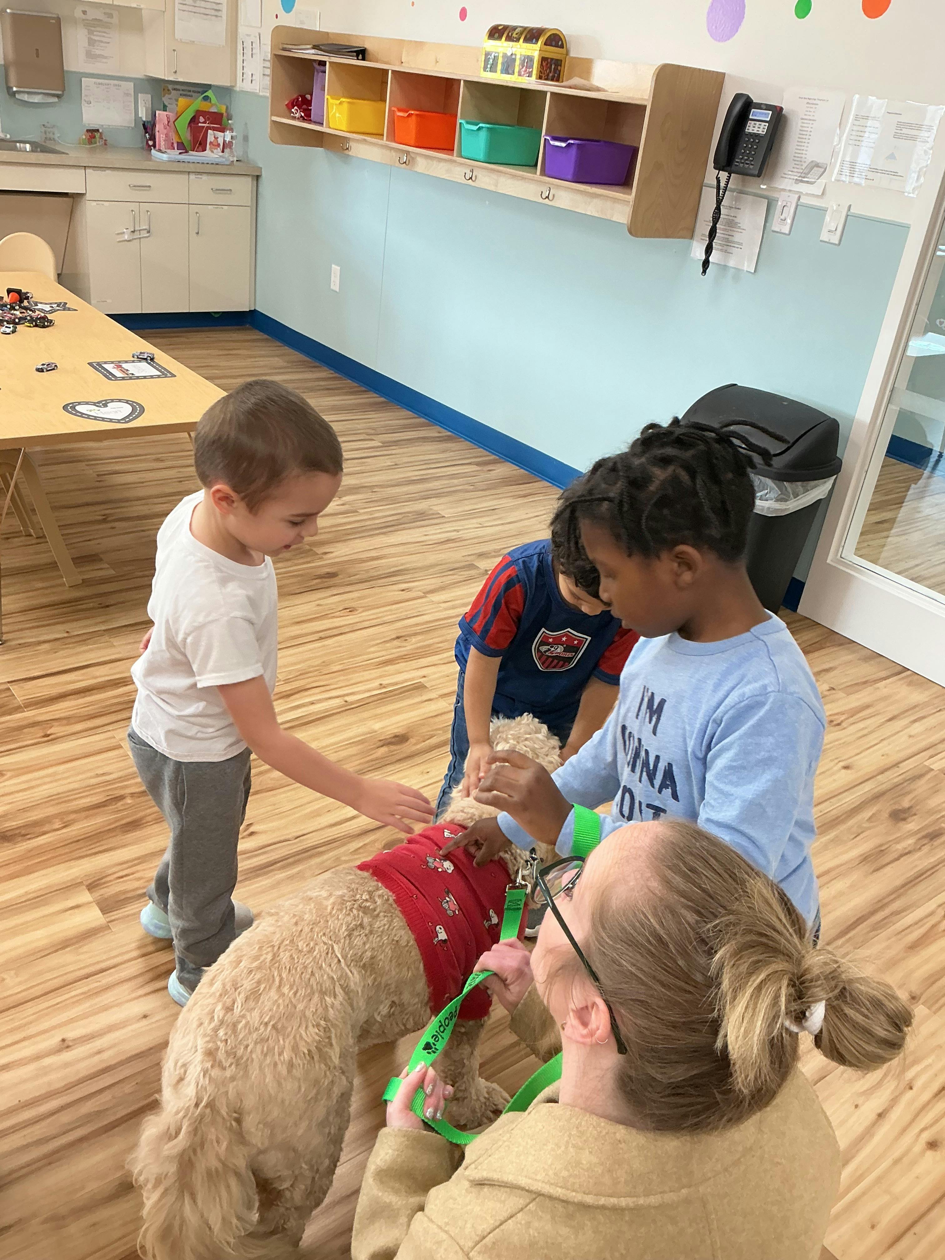 Teacher and two children petting a dog in a classroom