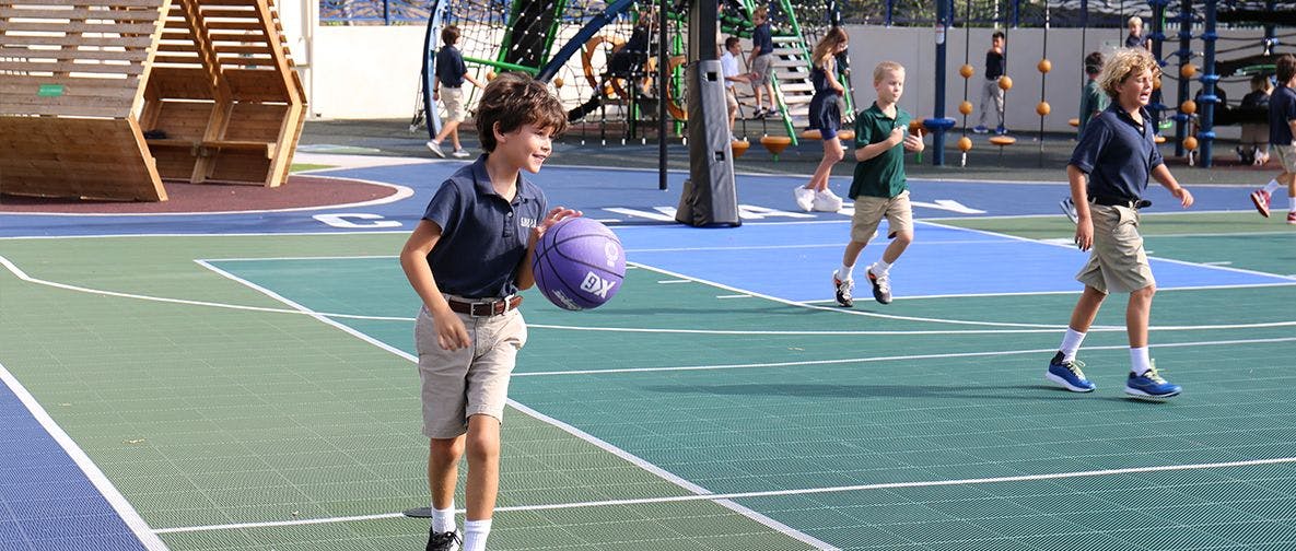 Child in uniform playing with a purple basketball on an outdoor court