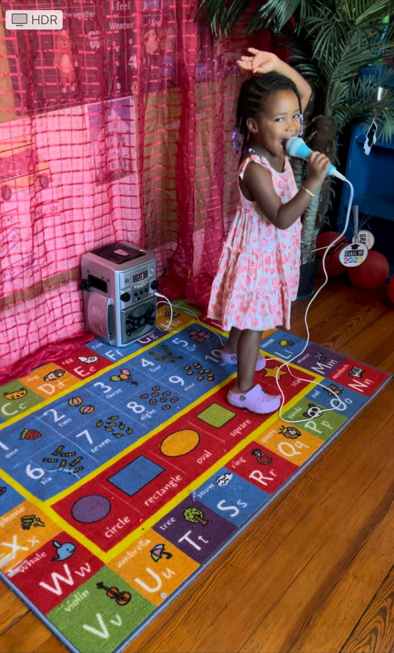 Child singing into a microphone on a colorful alphabet rug