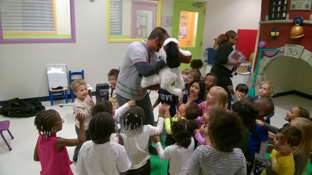 Person with a puppet surrounded by children in a classroom