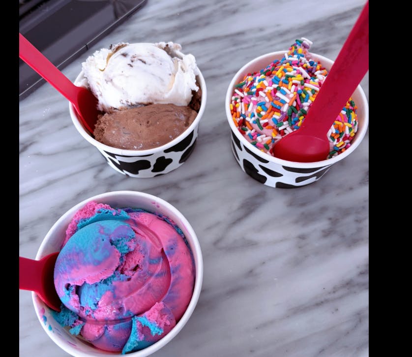 Three cups of ice cream with spoons, spoons including a cup with sprinkles and a cup with swirled blue and pink ice cream