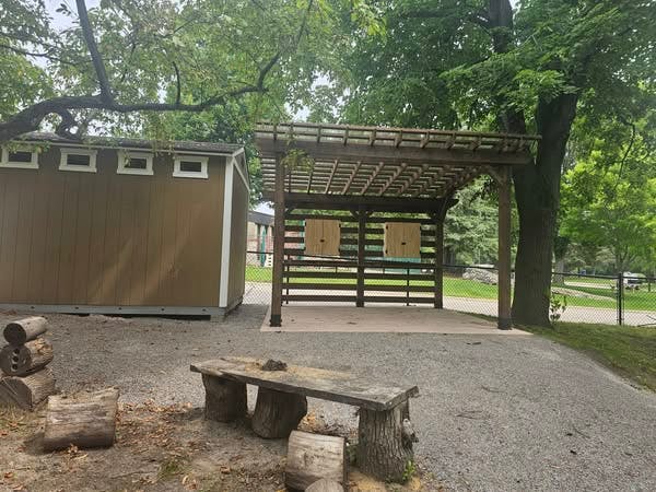 Brown shed and wooden pergola with benches and logs on a gravel ground