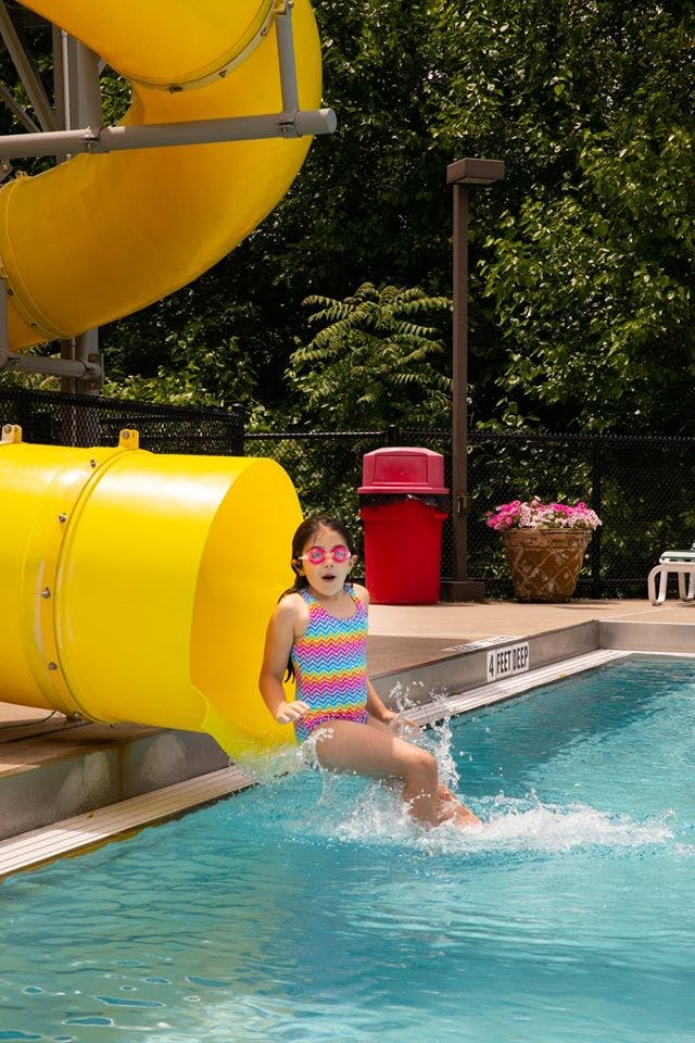 Child sliding out of a yellow water slide into a swimming pool