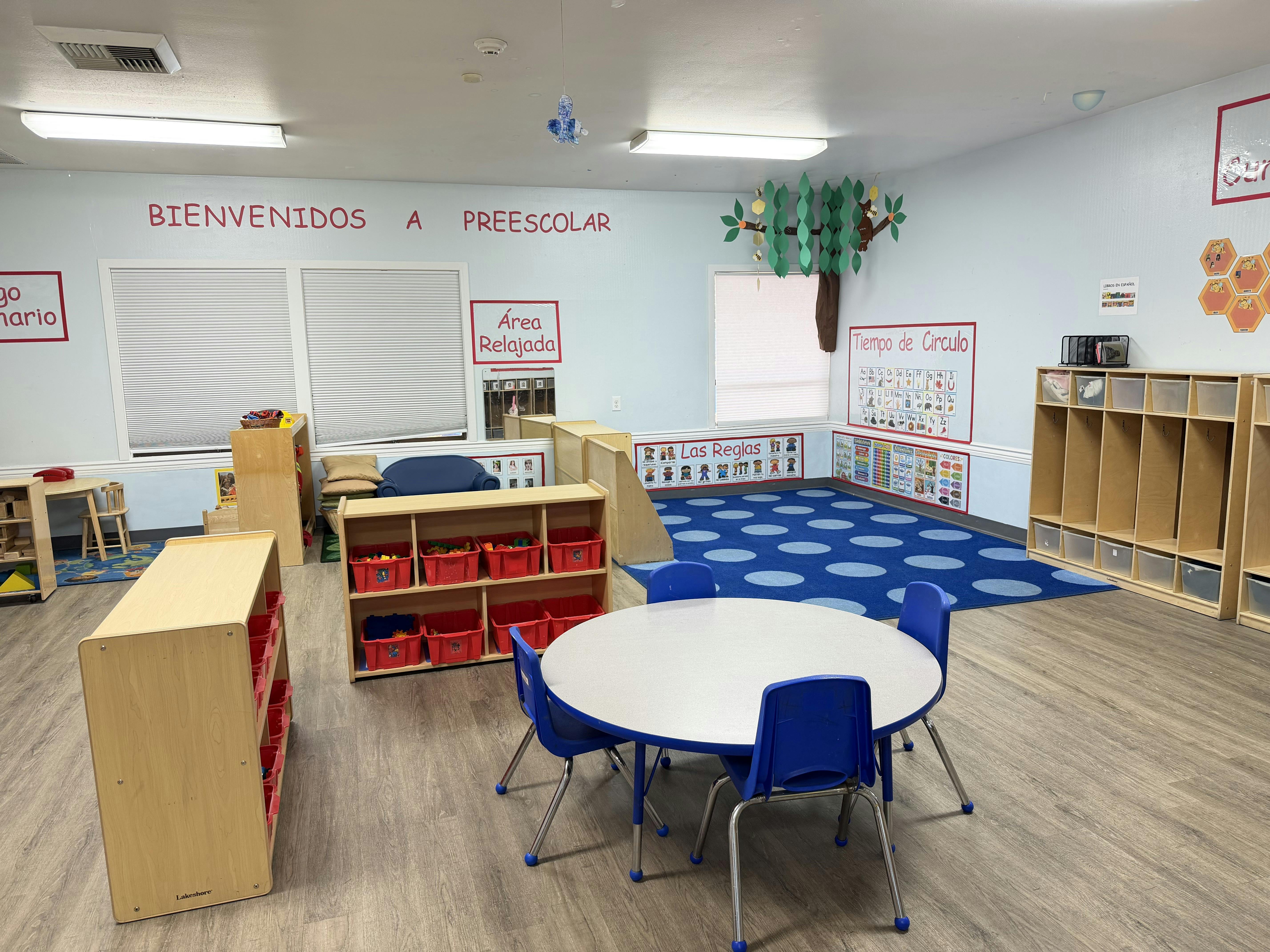 Empty preschool classroom with small tables and chairs and educational wall signs