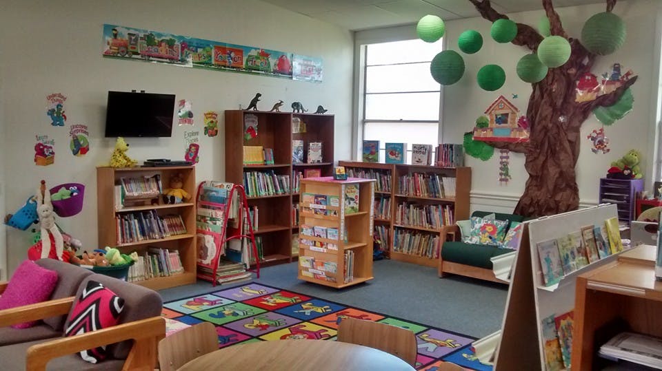 Children's library with bookshelves, colorful rug, and tree mural