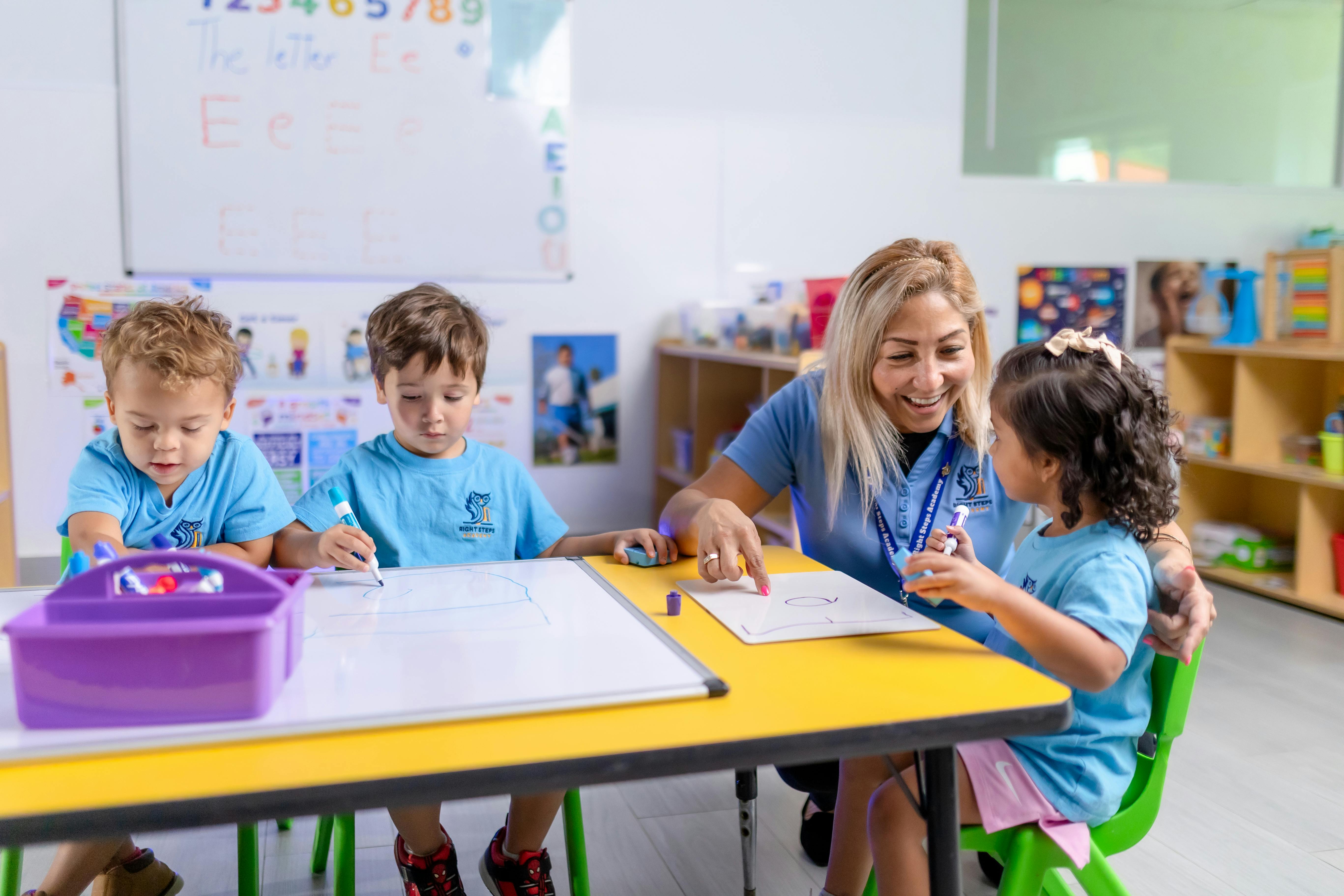 Teacher and three children drawing on whiteboards in a classroom