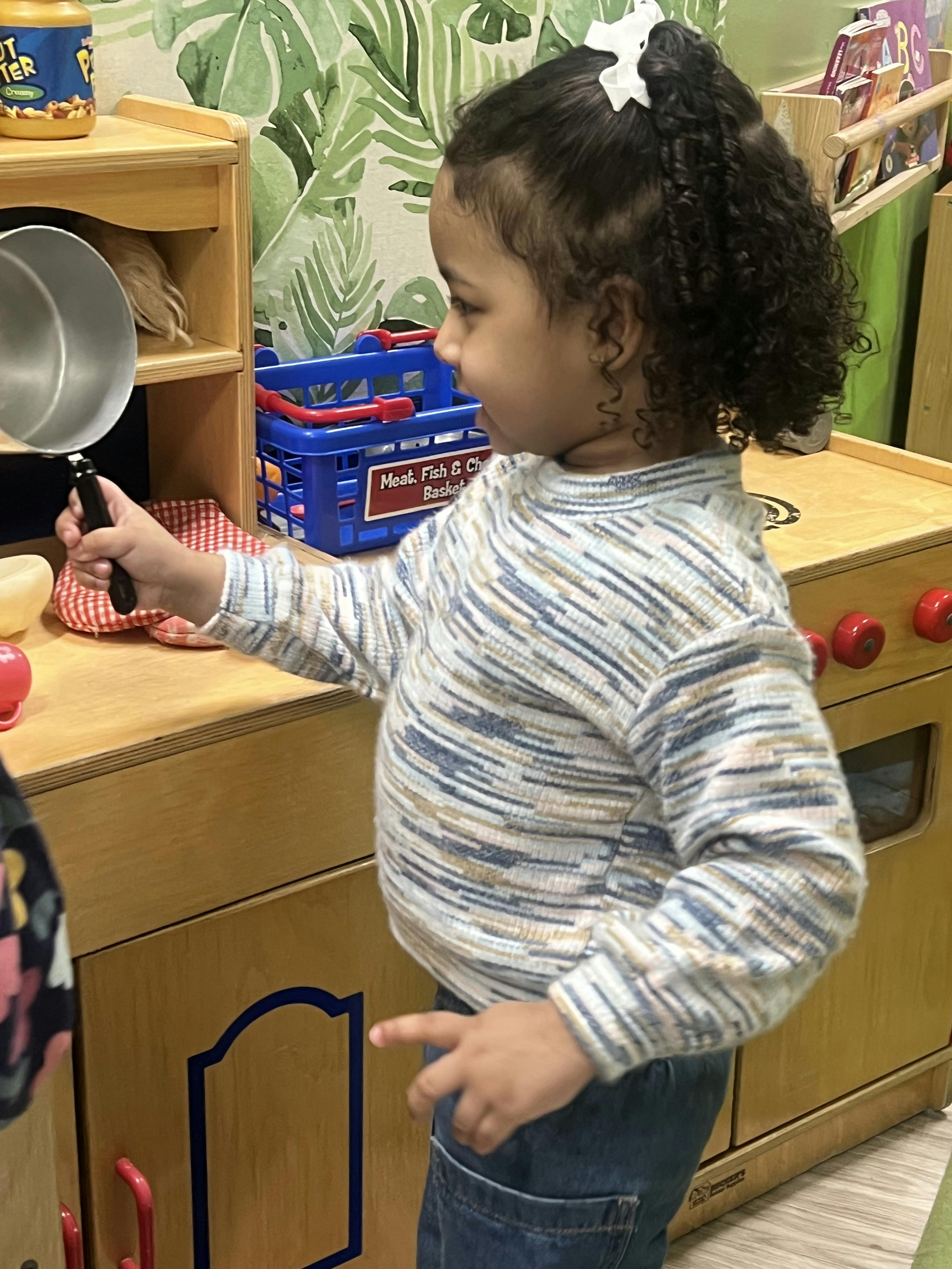 child playing with a toy pan in a play kitchen