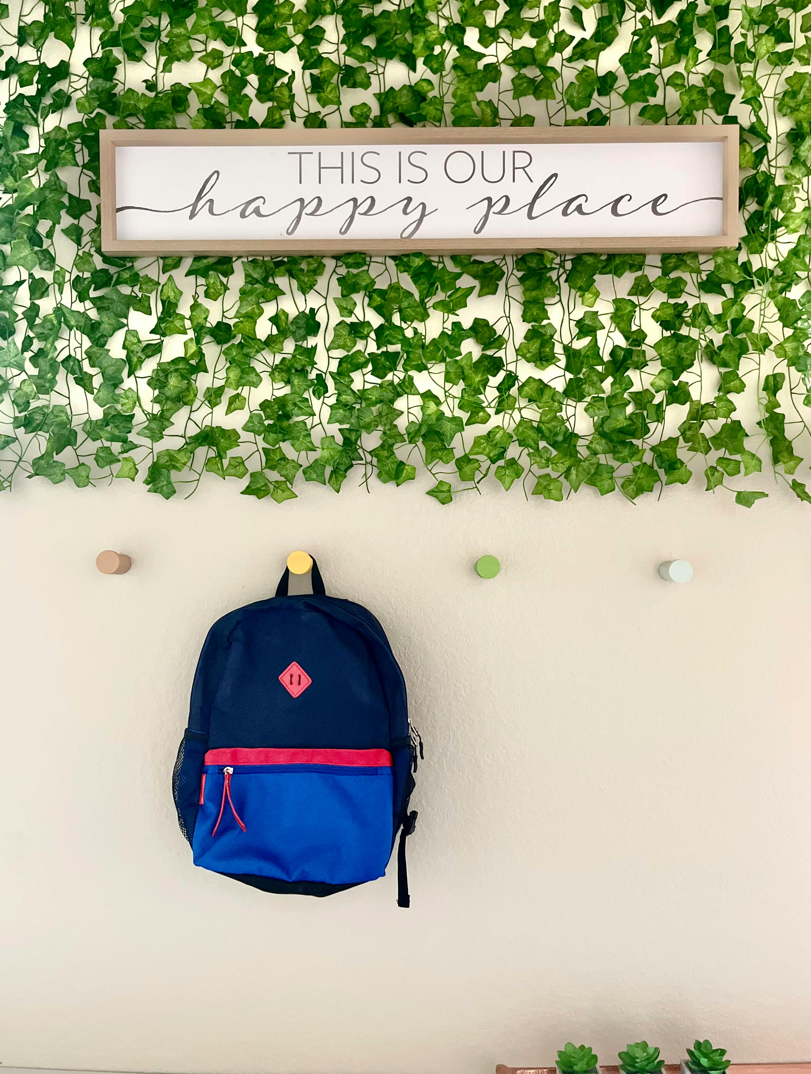 Backpack hanging on a wall with a sign that reads "THIS IS OUR happy place"