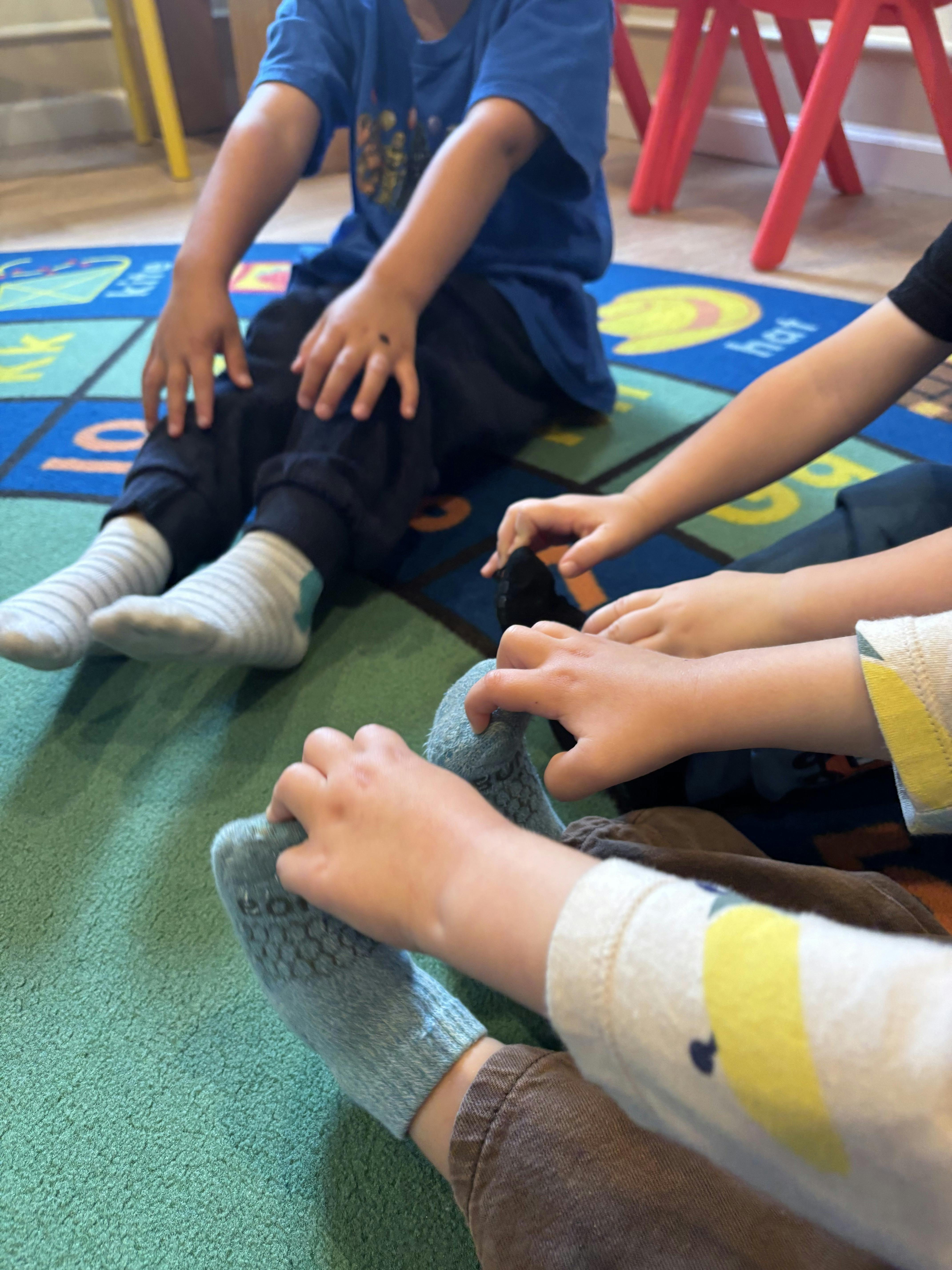 Children sitting on a classroom rug touching their socks