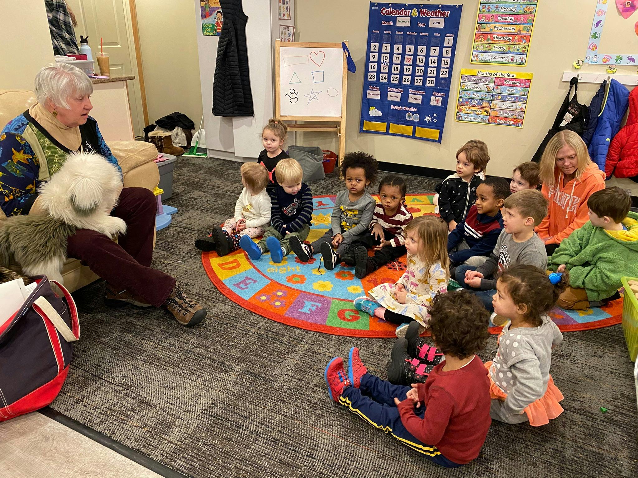 Person with a dog sitting on the floor with a group of children