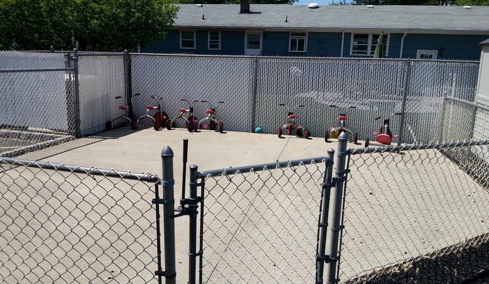 Tricycles parked against a fence in an outdoor play area