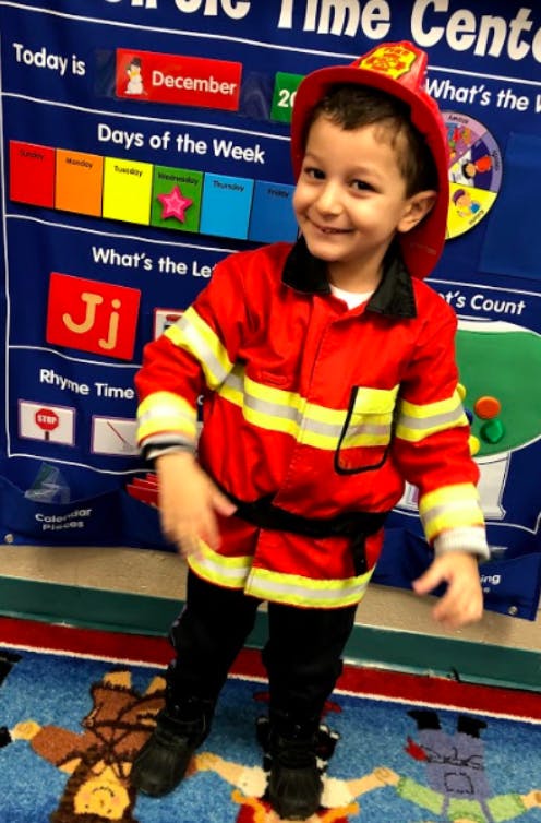 Child in a firefighter costume standing in front of a classroom calendar