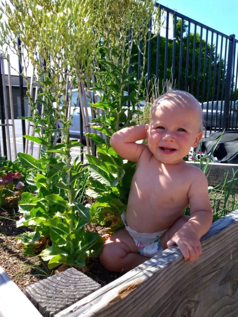 Child in a diaper sitting in a garden bed