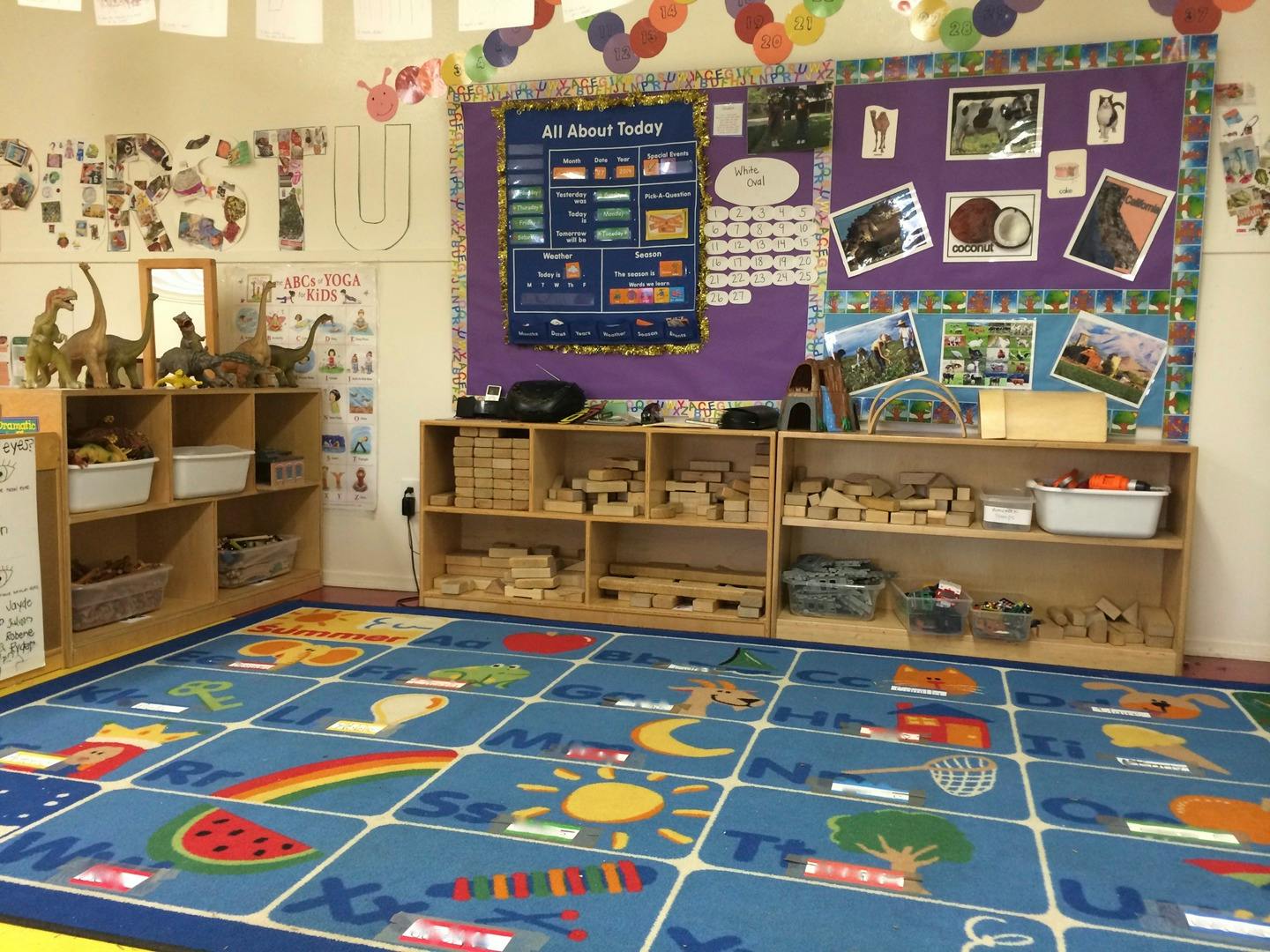 Classroom with a blue alphabet rug, shelves of toys, and bulletin boards