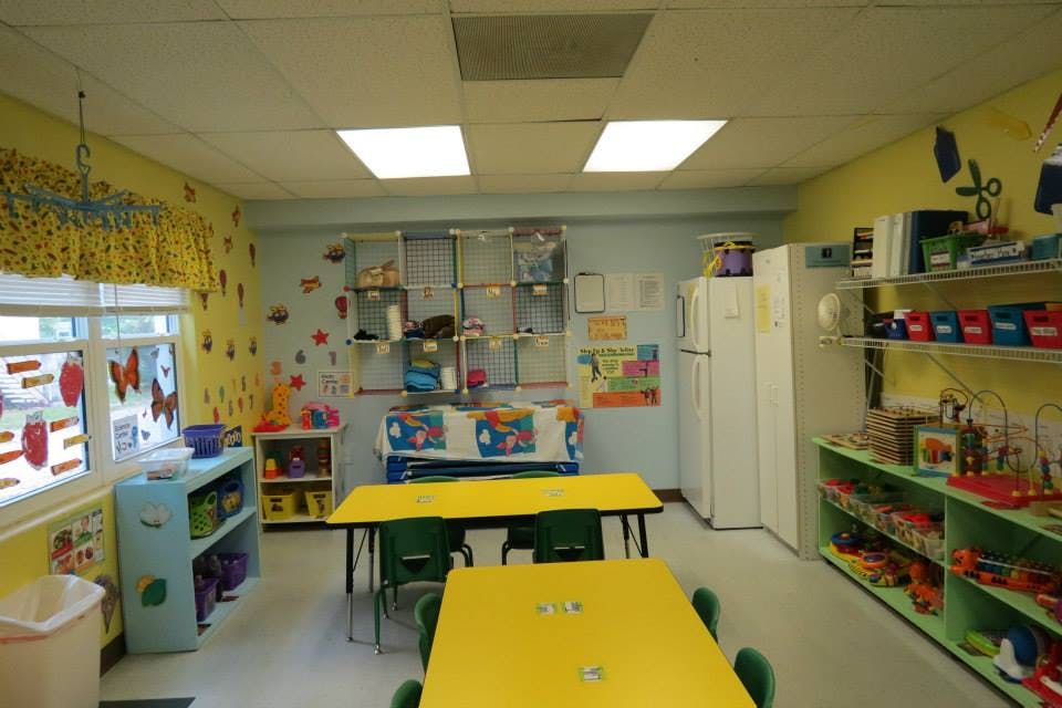 Classroom with yellow tables and chairs, shelves with toys, and decorated walls