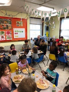 Children and adults eating at tables in a classroom