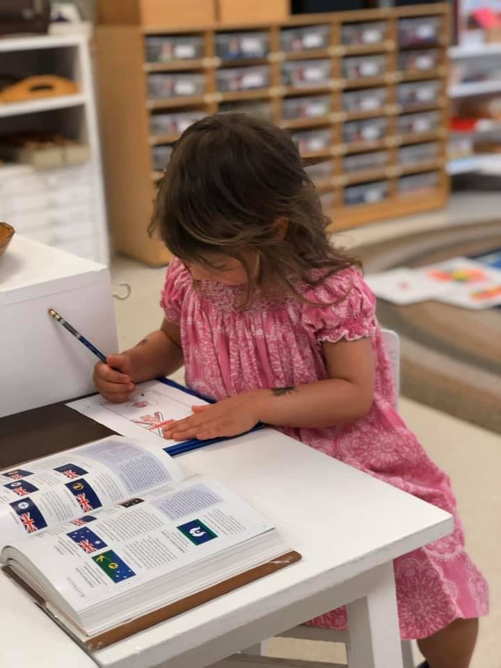 Child drawing at a desk with an open book