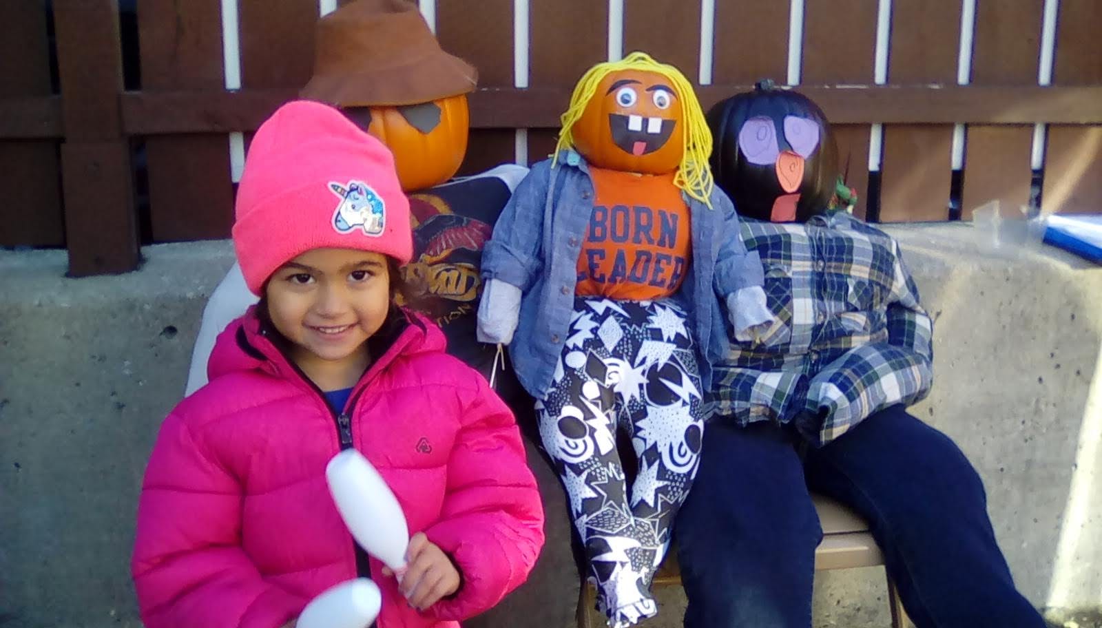 Child in pink coat and hat with scarecrows