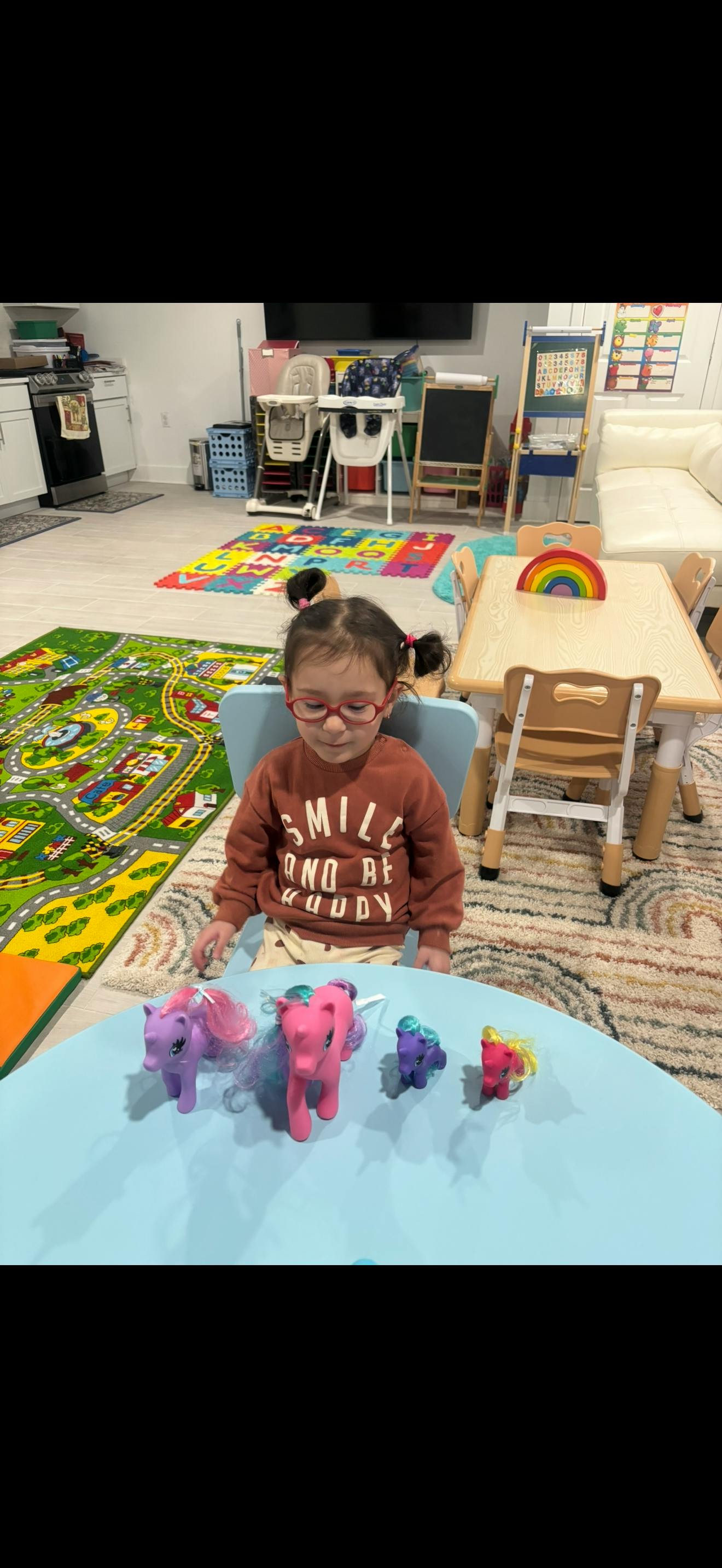 Child in glasses playing with My Little Pony figures on a blue table