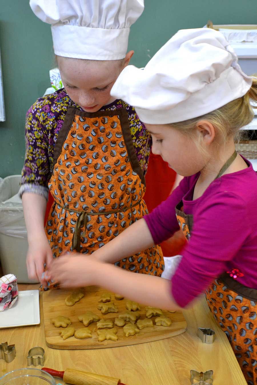 Two children in chef hats and aprons making cookies