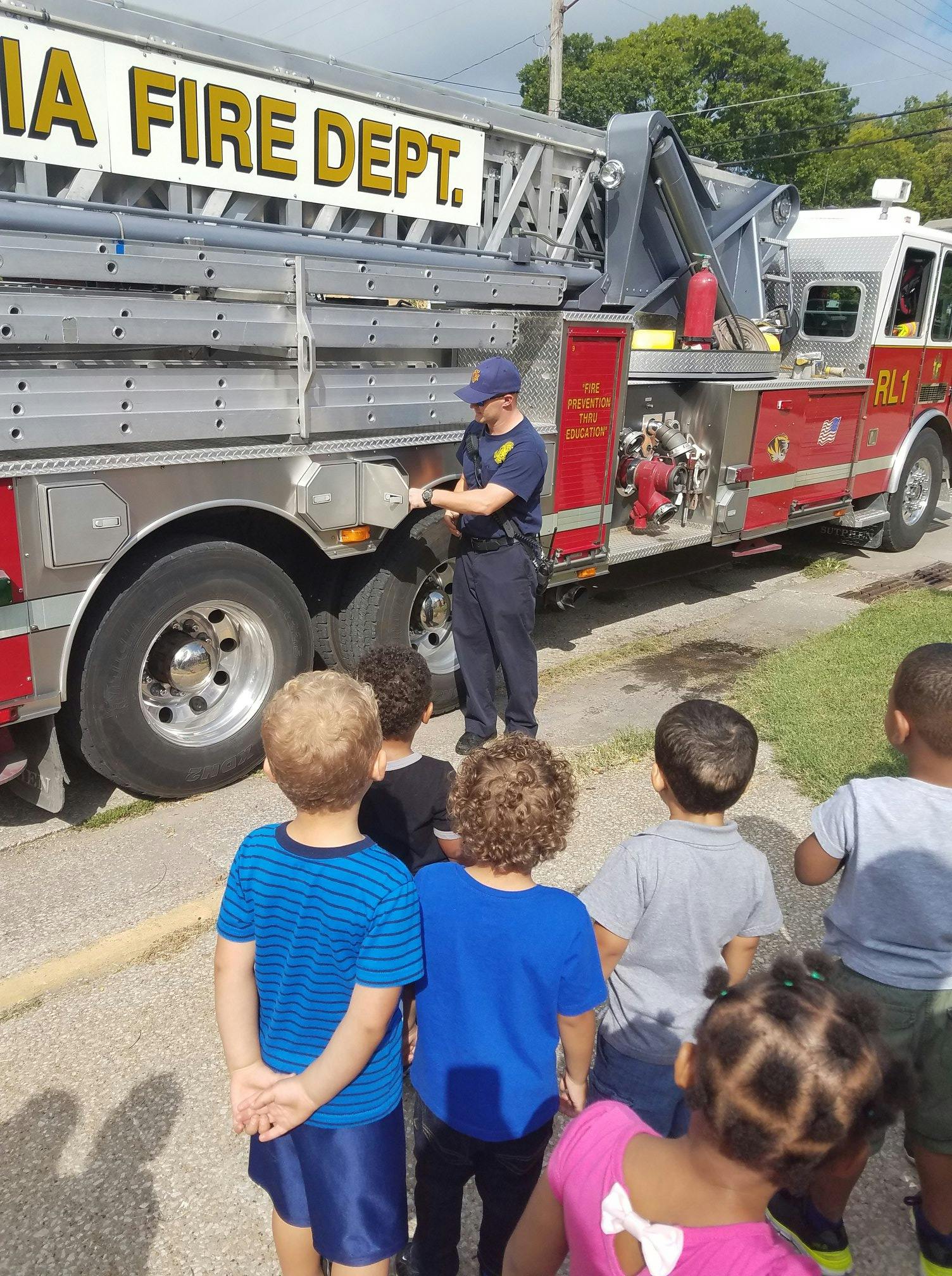 Person in uniform showing a fire truck to a group of children