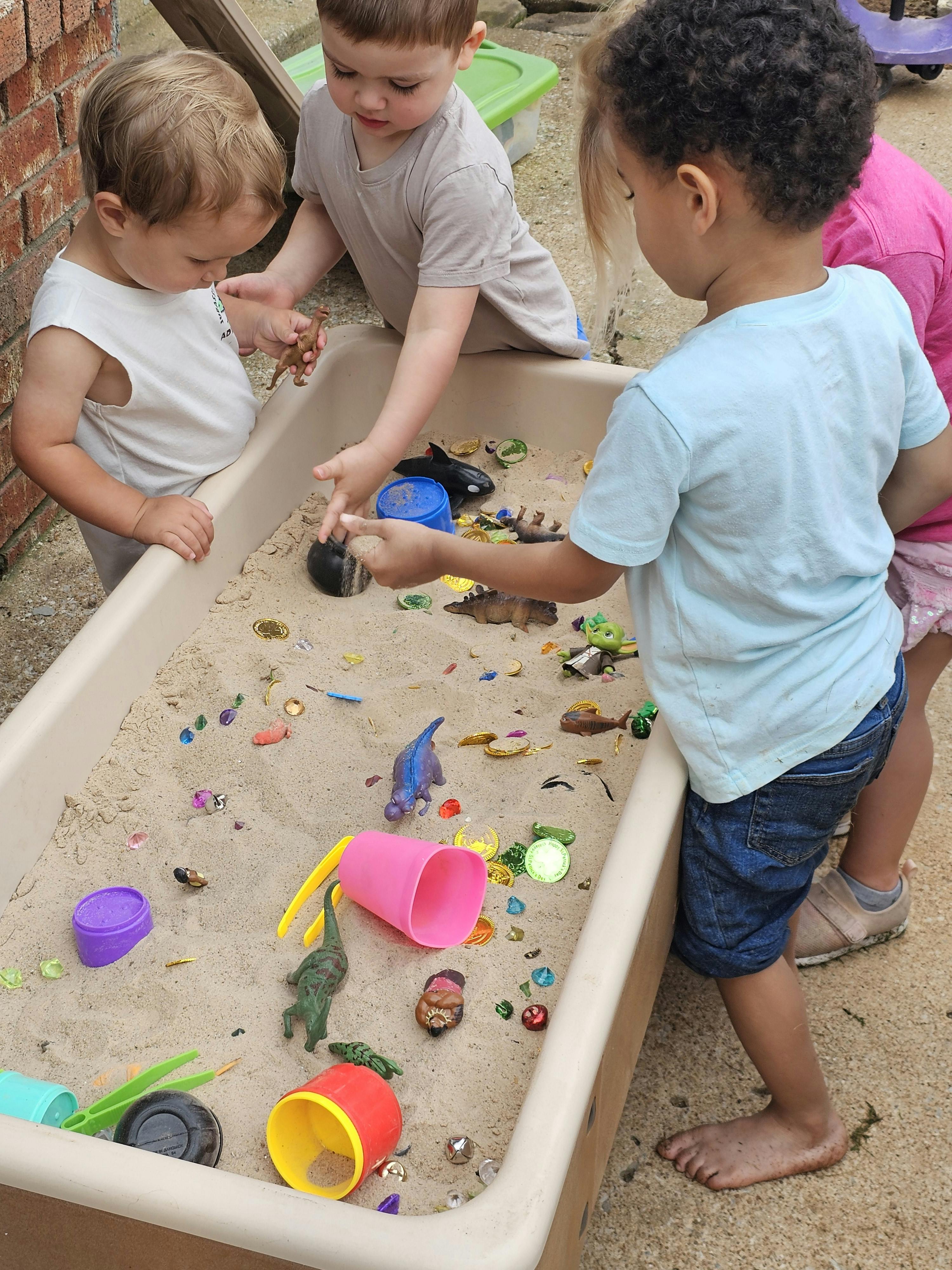 Three children playing in a sand table with toys