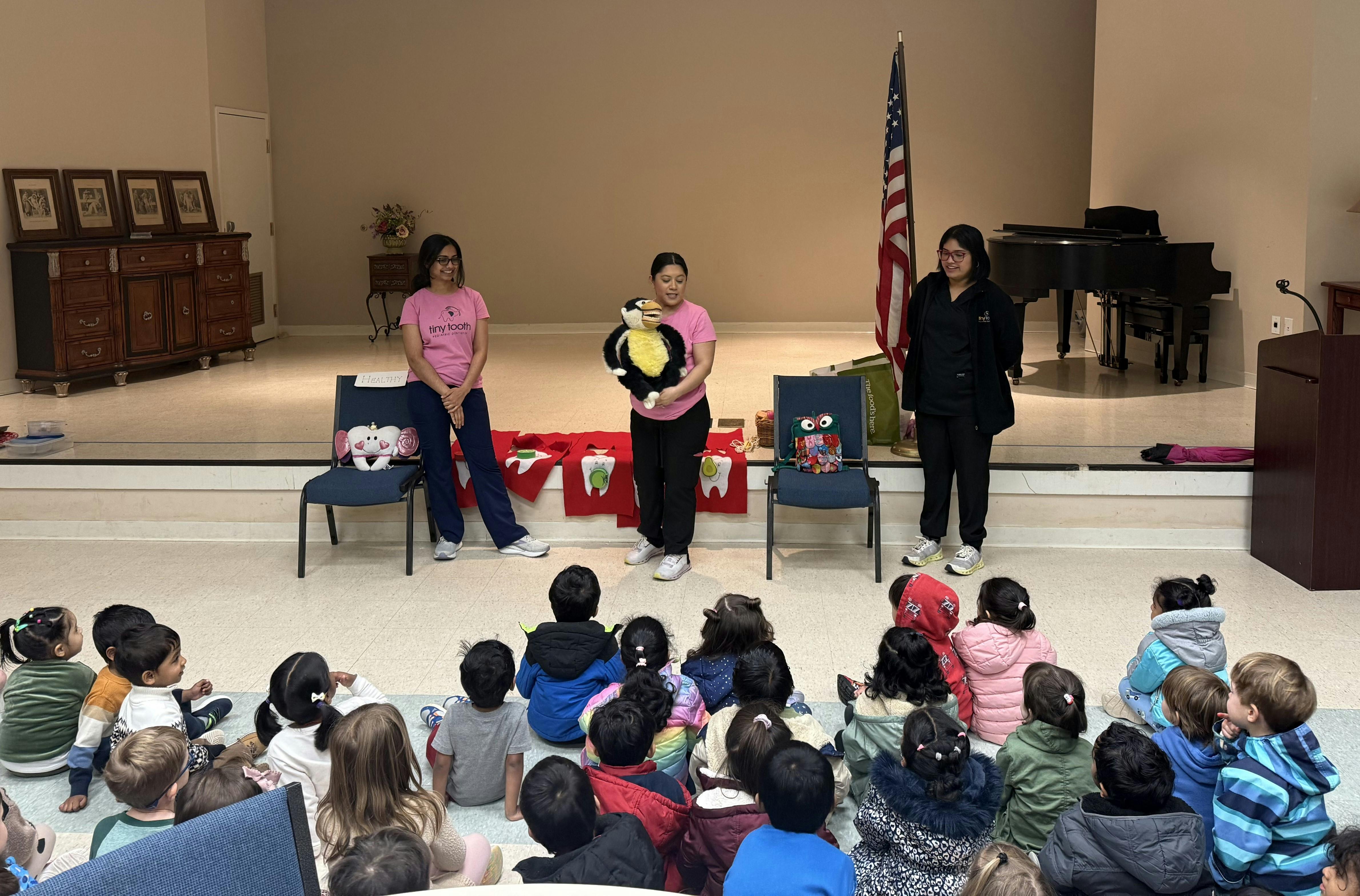 Three people presenting to a group of children seated on the floor