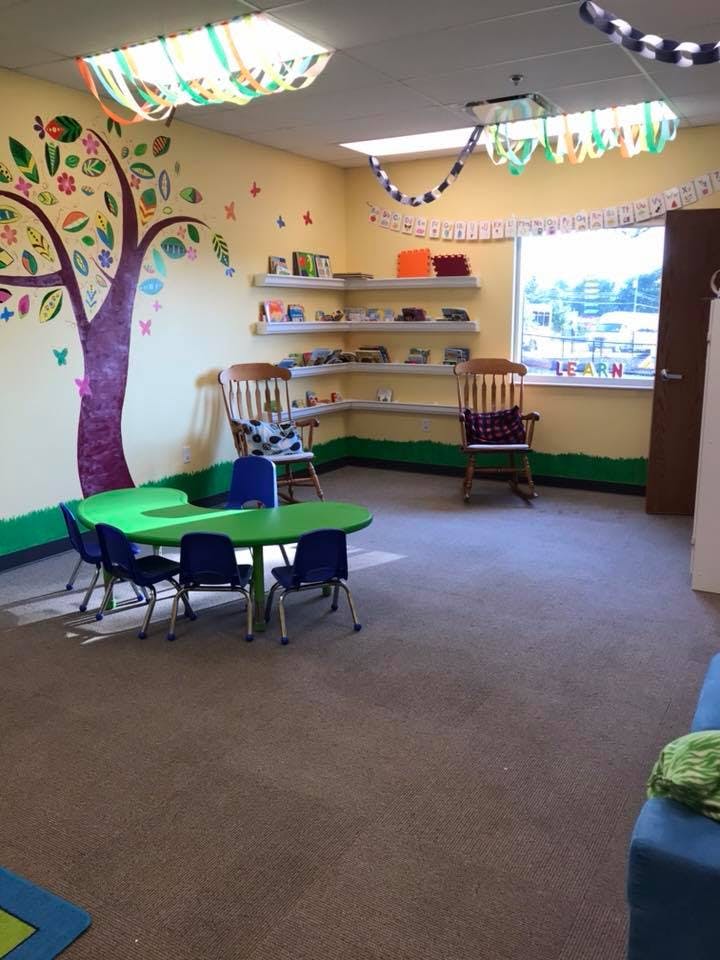 Classroom with a green table and blue chairs, shelves, and a tree mural