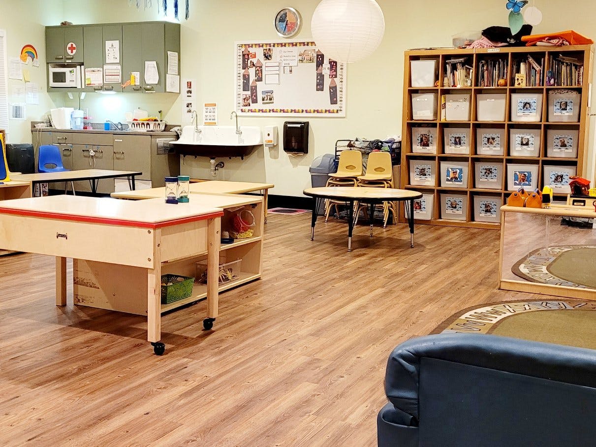 Empty classroom with tables, chairs, a sink, and storage cubbies