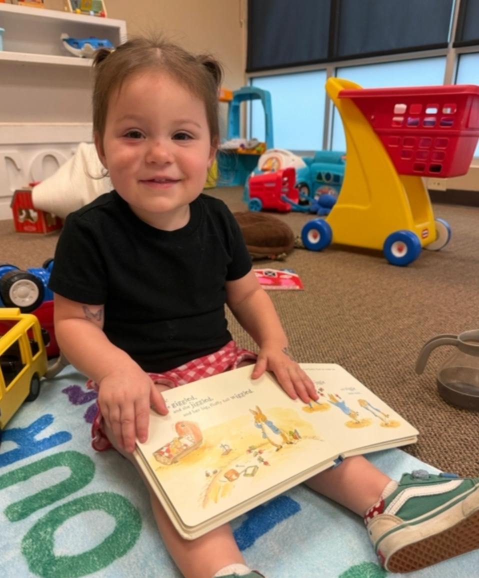 Child sitting on the floor reading an open storybook in a play area