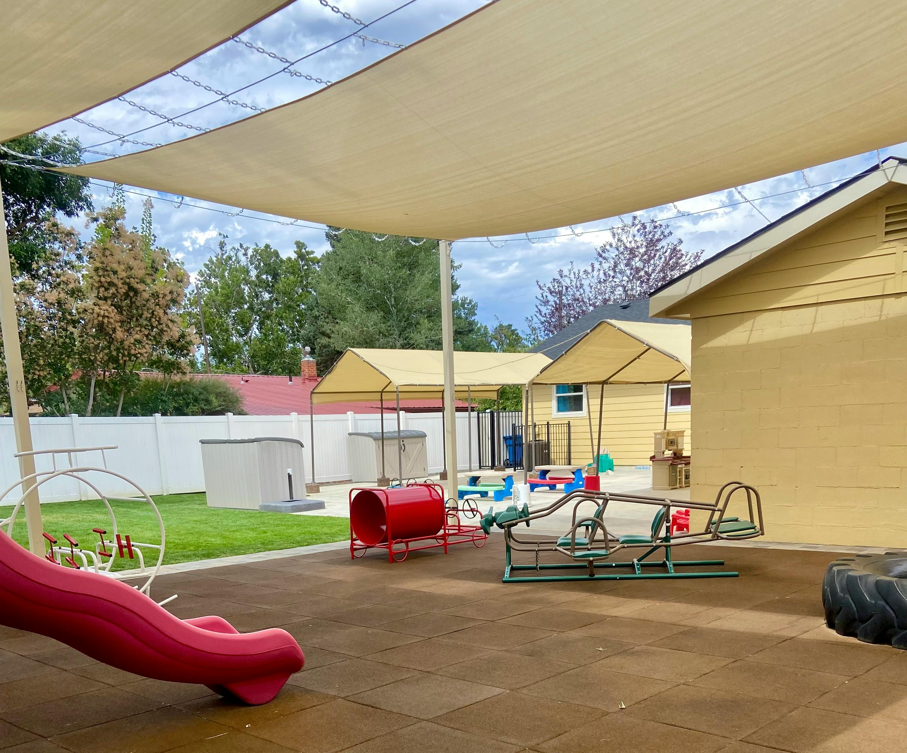 Playground with a red slide, red tunnel, and green seesaw under a shade sail