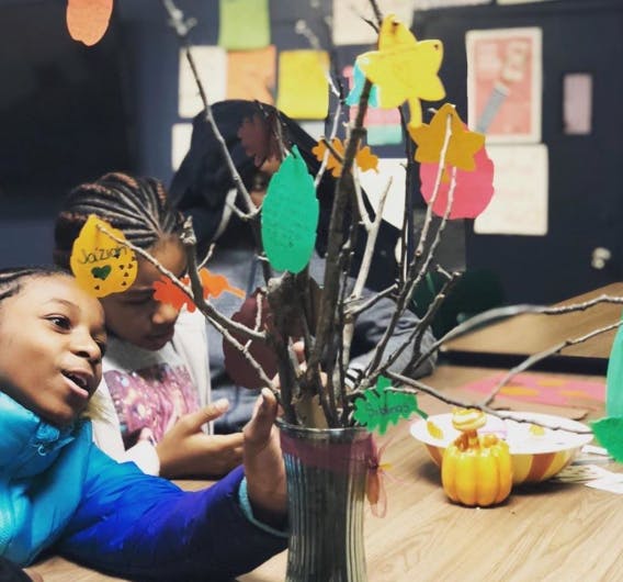 Two children looking at a vase with branches decorated with paper leaves