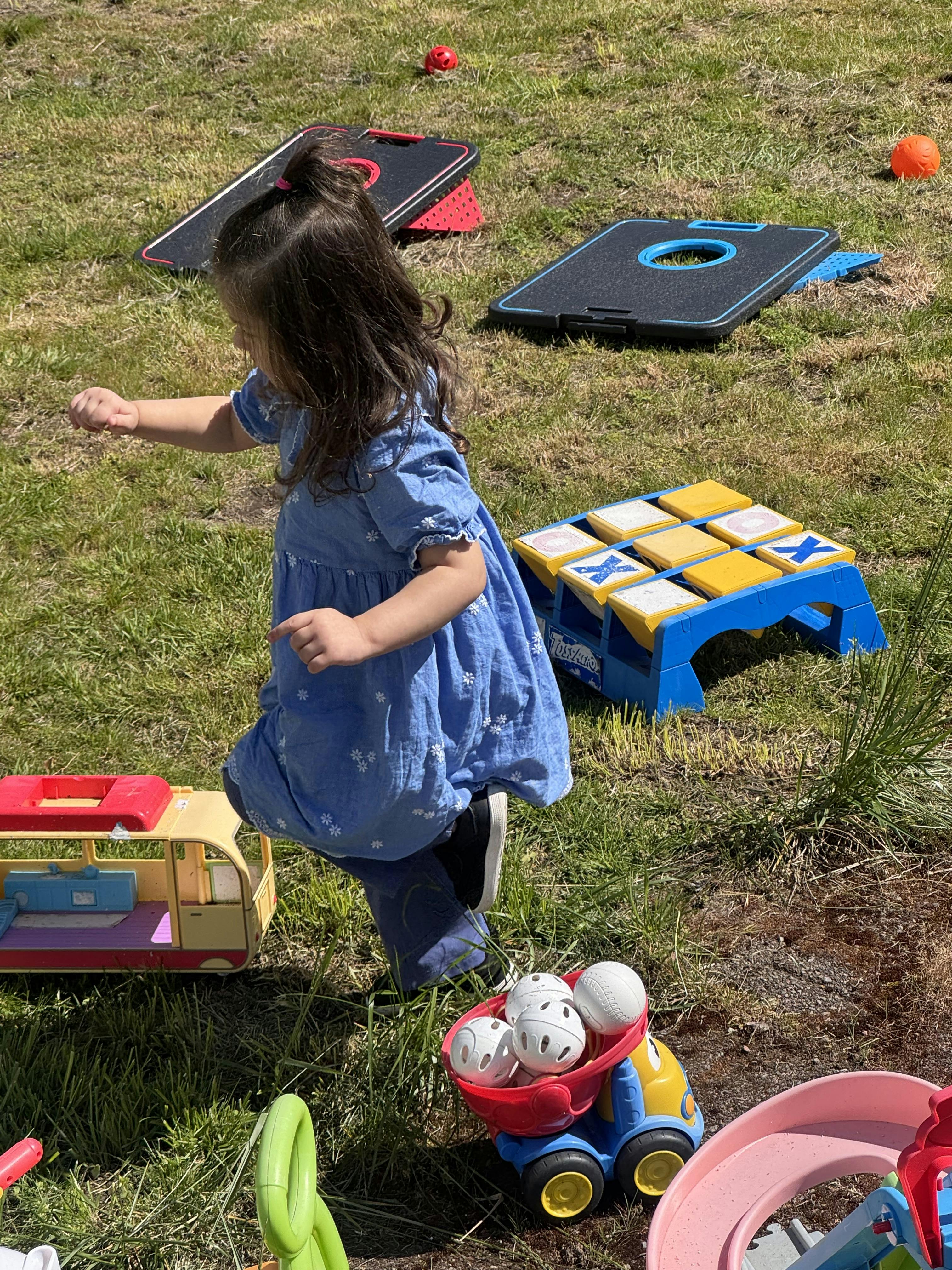 Child in blue dress playing with toys on grass