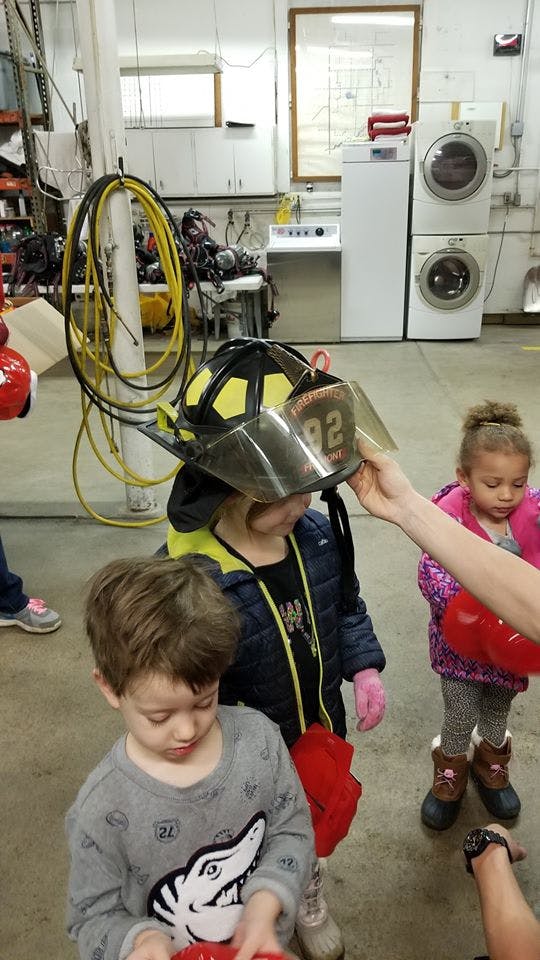Person helping a child try on a firefighter helmet
