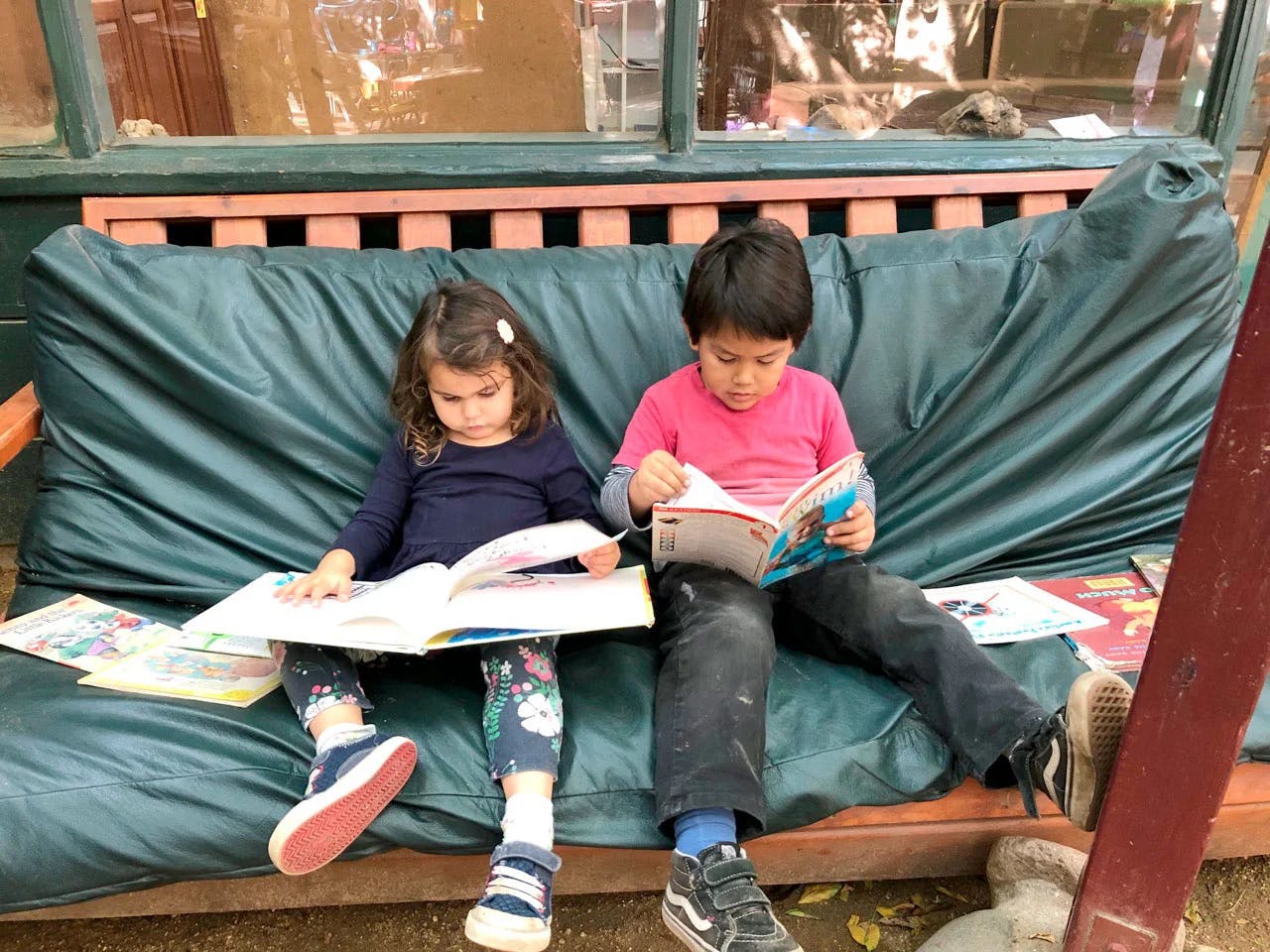 Two children sitting on a bench, each reading a book