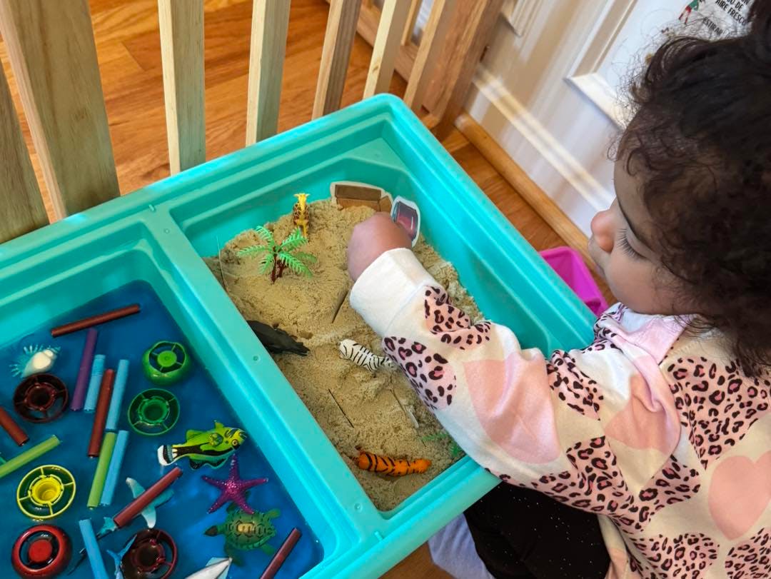 Child playing with a sensory table filled with sand, water, and toys