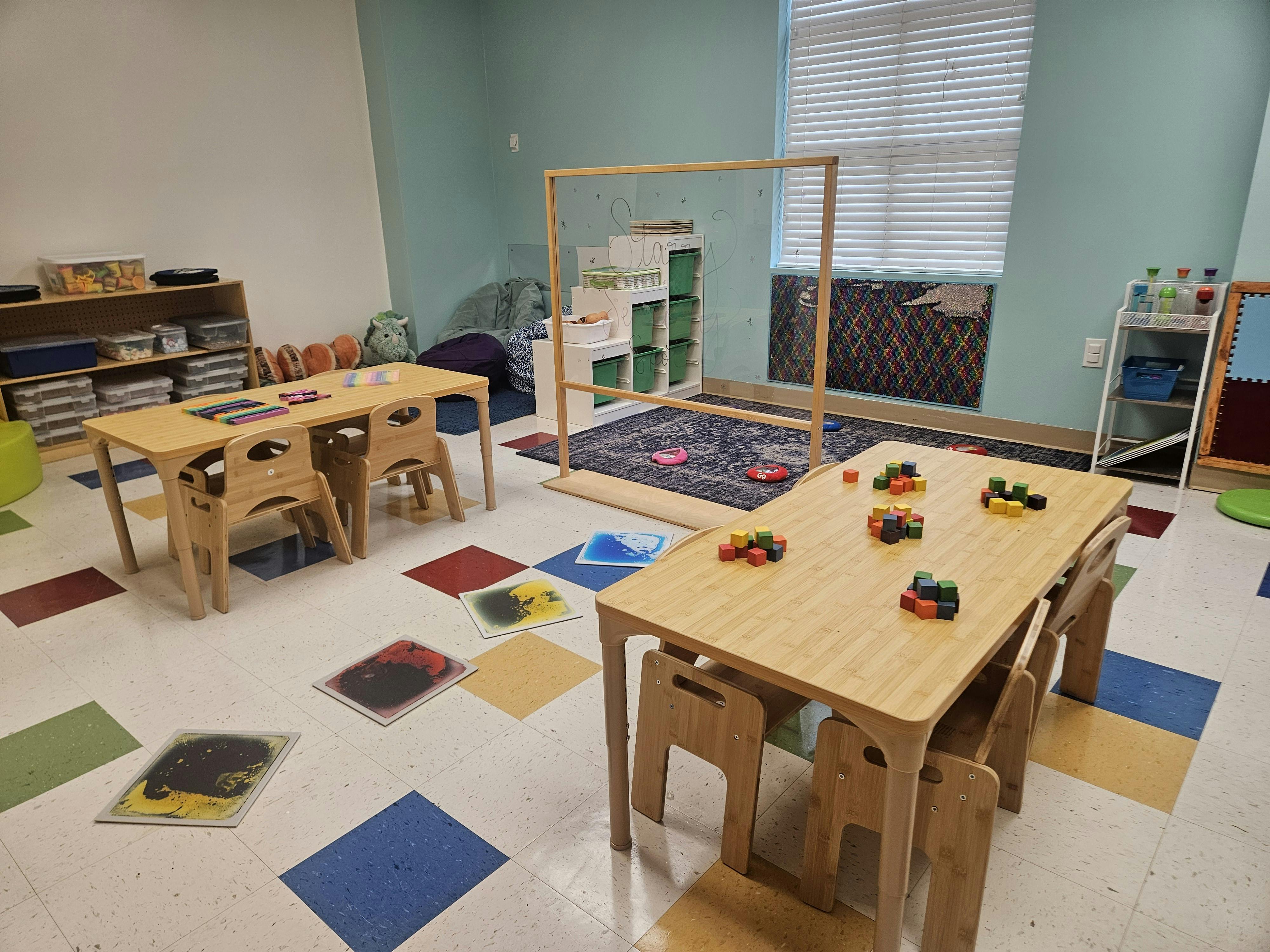 Classroom with small wooden tables and chairs, colorful floor mats