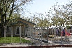 Small building behind a metal fence with trees and playground equipment