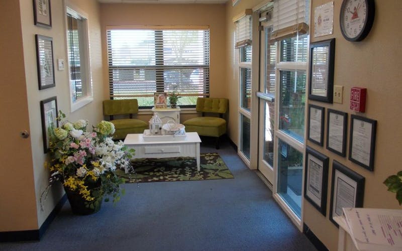 Waiting area with two green chairs, a white coffee table, and a large plant